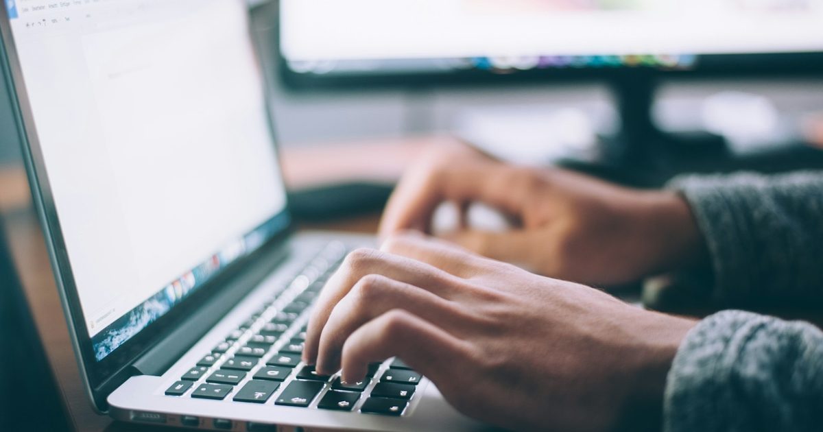 A person working on a modern laptop at a desk with a notebook