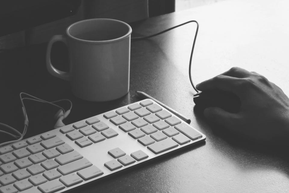 A hand at a desk beside a mug and keyboard