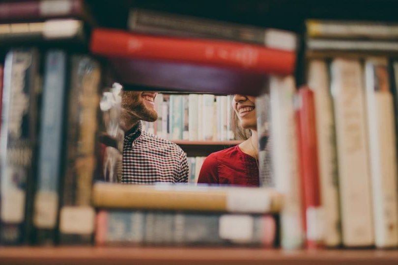 Two students seen through gaps in library bookshelves
