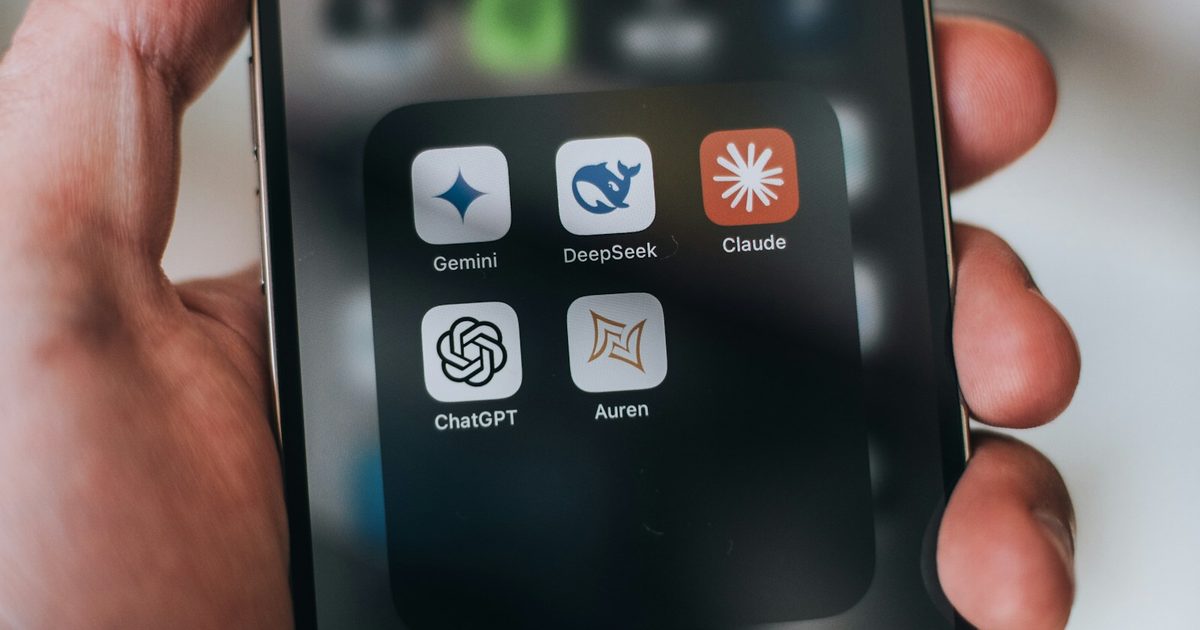 A hand holding a phone showing AI app icons including ChatGPT, Gemini, Claude, and DeepSeek