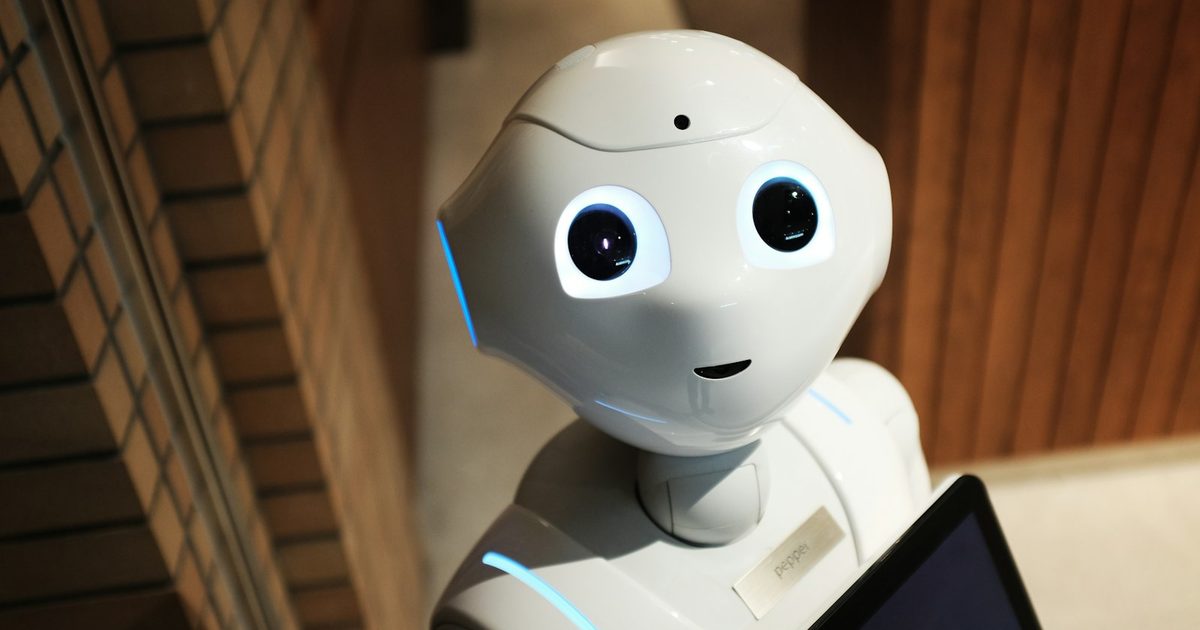 A small white robot standing against a plain wall, representing simple automation
