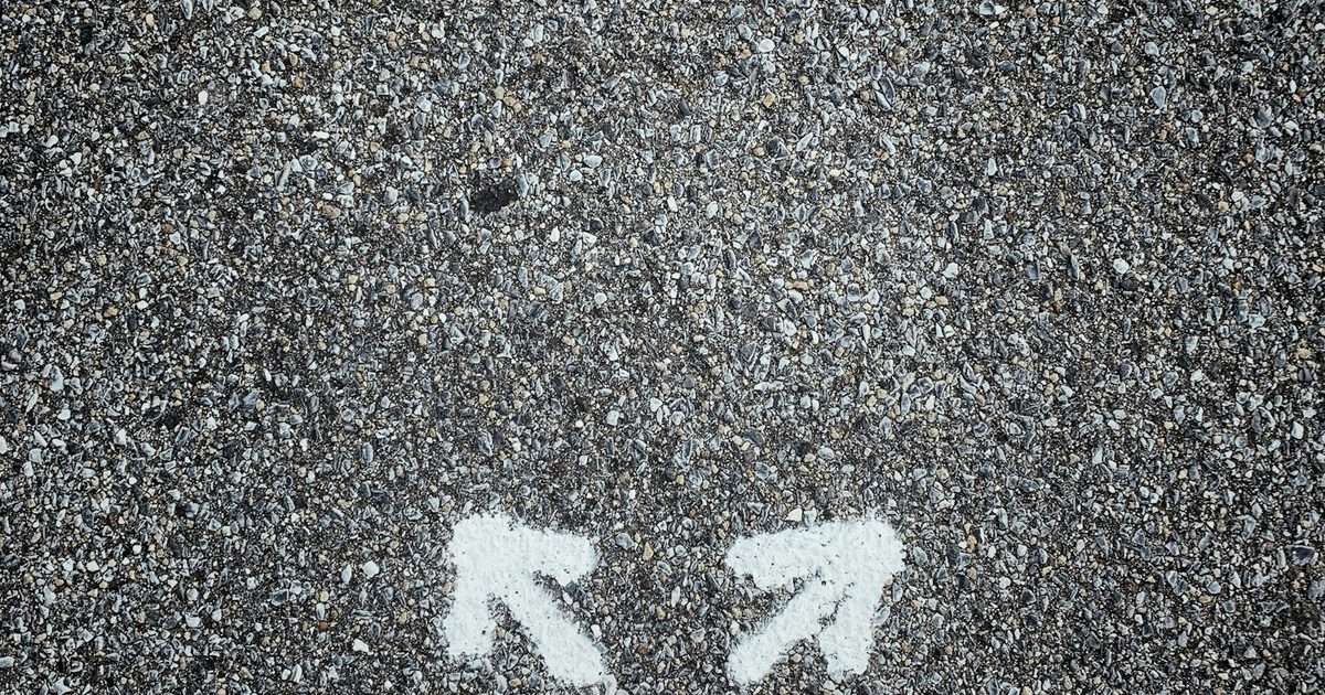 A person standing on pavement between two arrows pointing in opposite directions