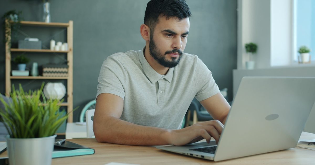 شابّ يركّز على لاب توب على مكتب منزليّ مرتّب