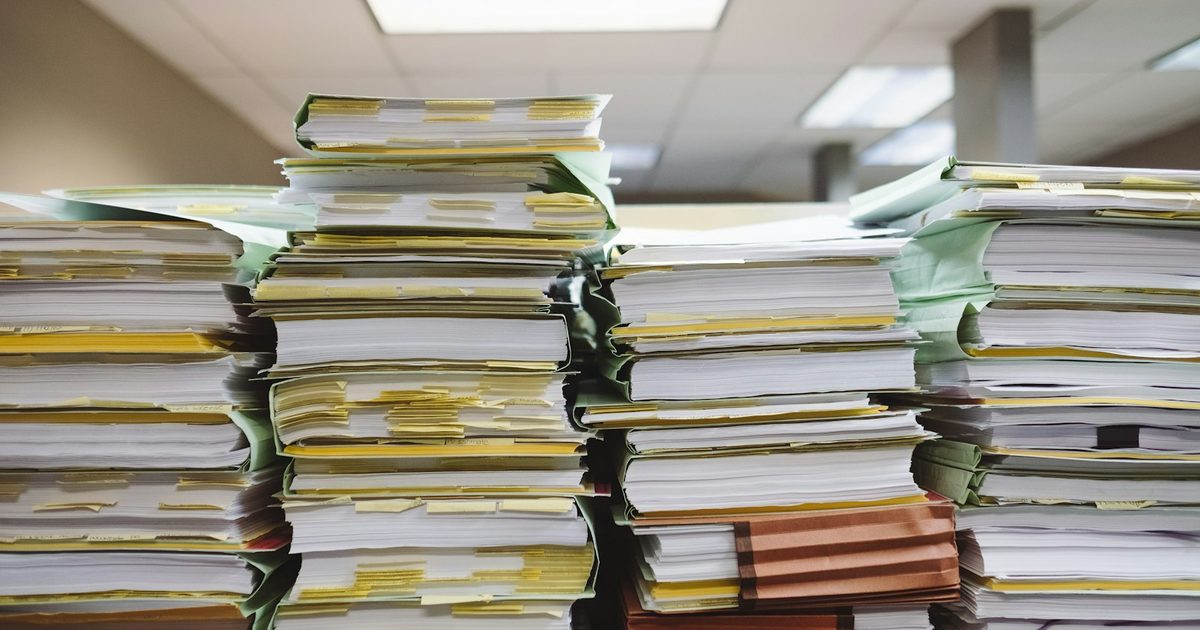 Stacked piles of paper documents and file folders on a desk