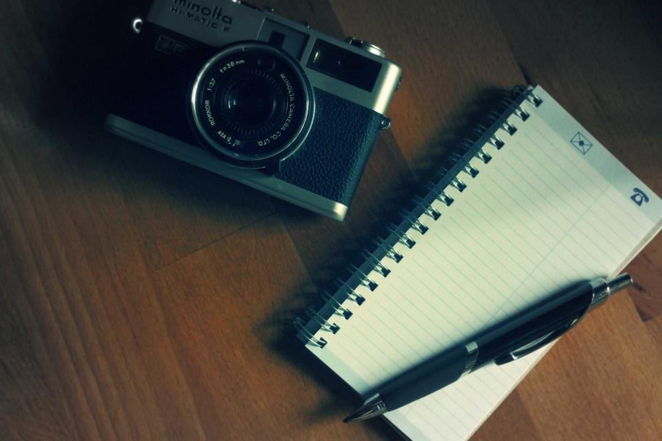 A film camera, notepad and pen on a wooden desk