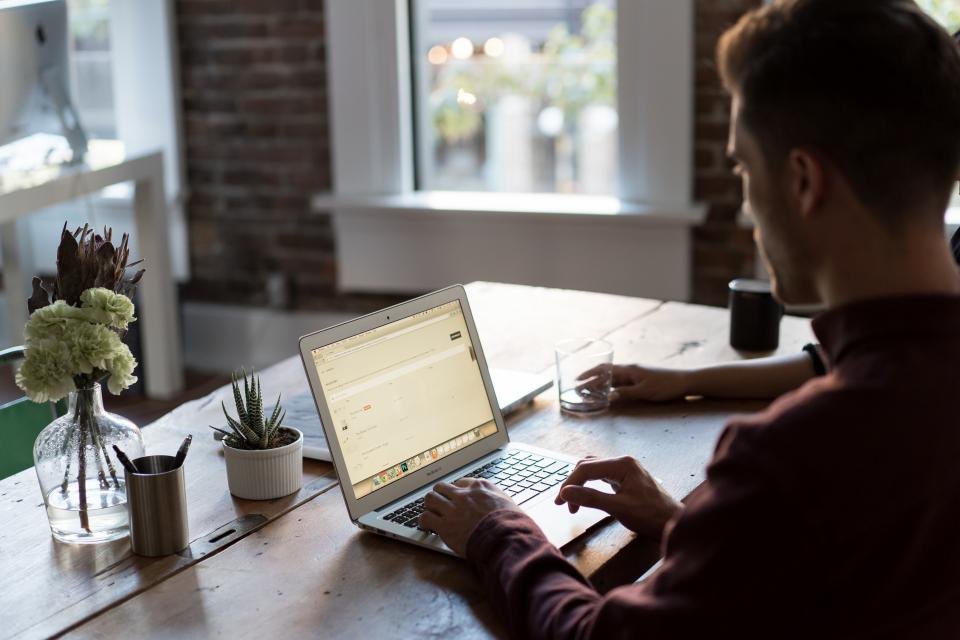 A person filling in a form on a laptop at a wooden desk