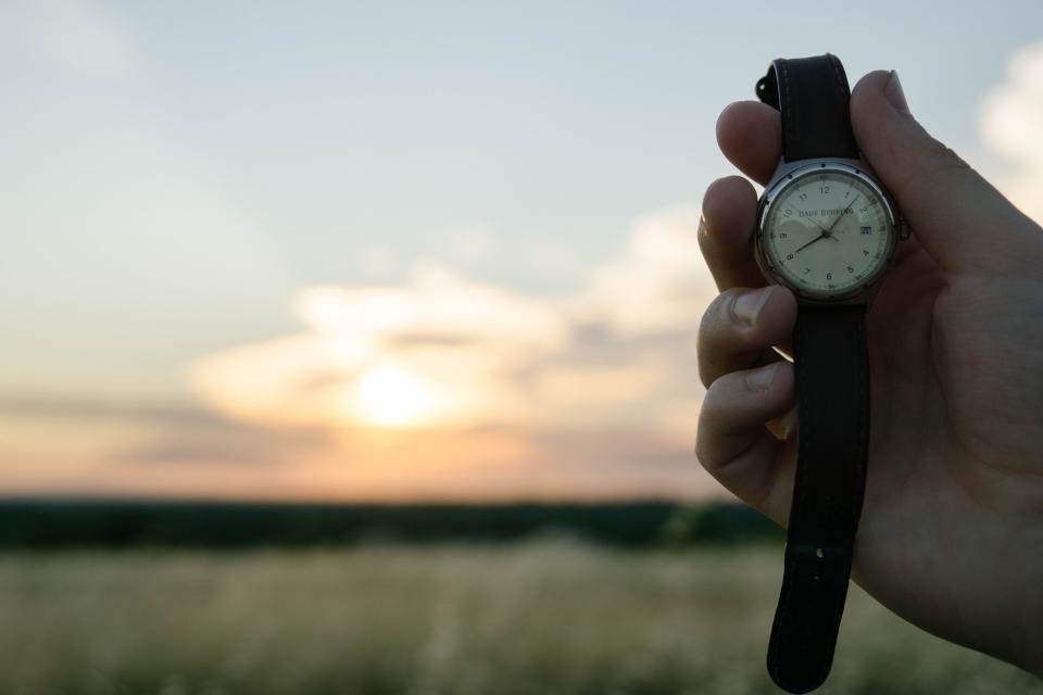 A hand holding a wristwatch against a sunset