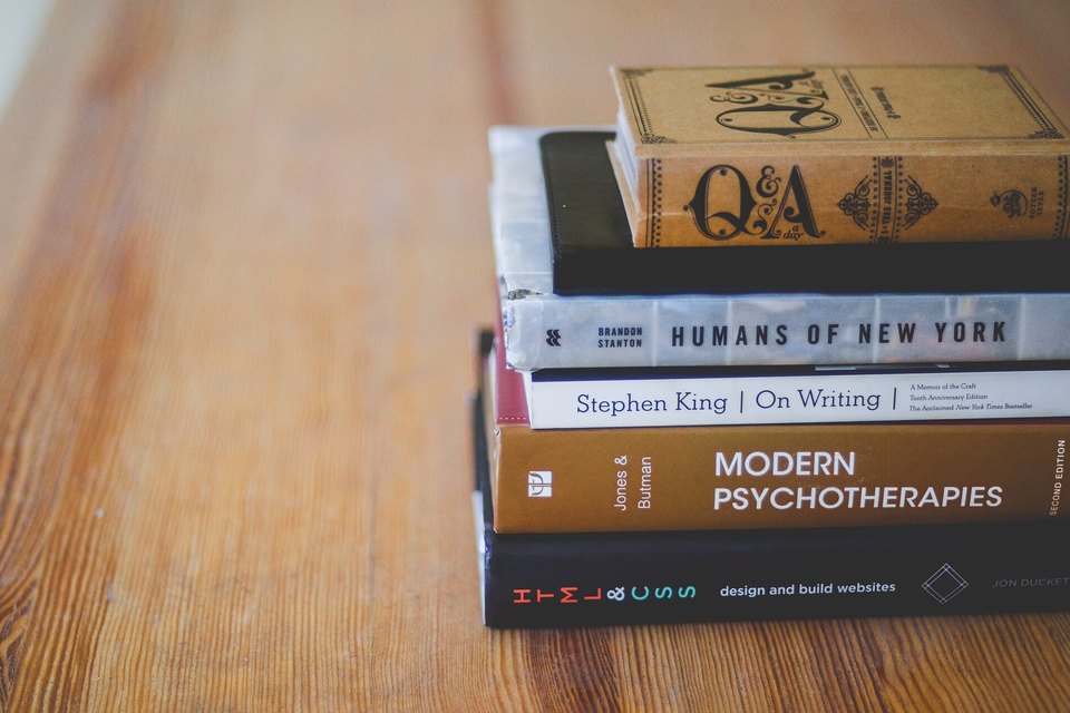 A stack of printed books resting on a wooden table